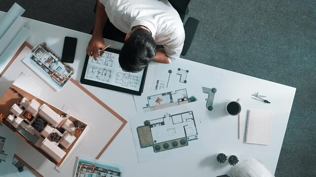 Top view of business man using tablet plan house design while sitting at meeting table with blueprint and equipment scatter around. Aerial view of civil engineer working at blueprint. Alimentation.