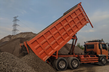 Heavy-duty dump truck unloads gravel at a construction site, creating a large pile of aggregate. © faiz_99