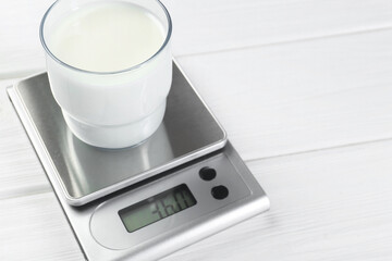 Kitchen scale with glass of milk on white wooden table, closeup. Space for text