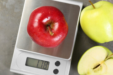 Kitchen scale with apple among ones on grey textured table, flat lay