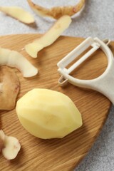 Fresh raw potato, peels and peeler on light grey table