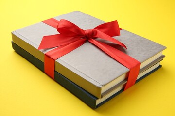 Books tied with red ribbon on yellow background, closeup