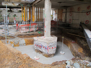 Column foundation underpinning and strengthening at a construction site with exposed foundation pile, concrete reinforcement, and support beams. Foundation repair and structural reinforcement. 