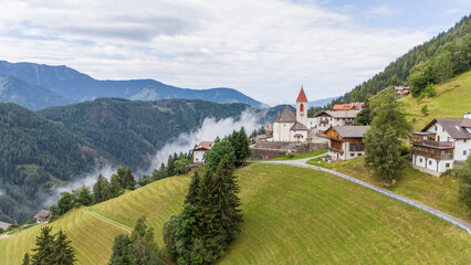 Aerial drone view of village, town Eores (Afers) near Bressanone (Brixen). Cloudy summer day. View on the Church of San Giorgio in the centre. Idyllic mountain village in the Italian Dolomites.