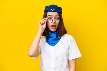 Airplane stewardess Ukrainian woman isolated on yellow background with glasses and surprised