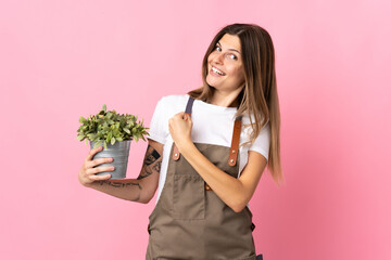 Gardener woman holding a plant isolated on pink background celebrating a victory