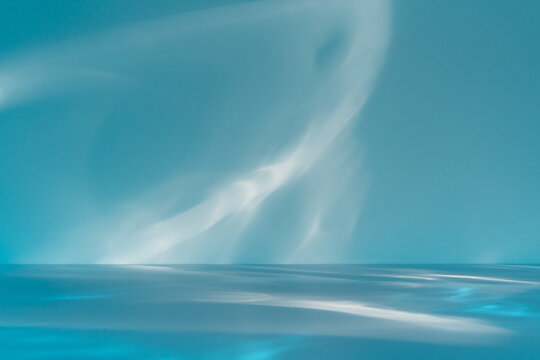 Minimalist abstract light blue background for product presentation with sunny light and abstract shadow or water reflection on wall.
