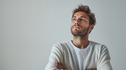 Fototapeta premium A man with a thoughtful expression, standing with his arms crossed against a white background, embodying contemplation