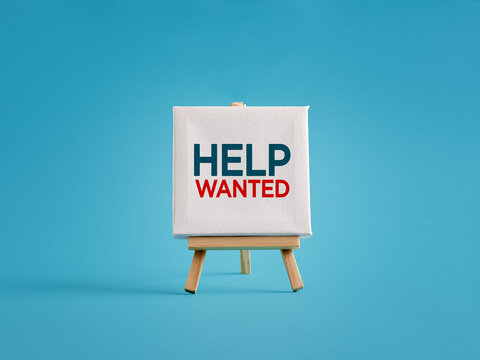 Small wooden easel with help wanted sign displaying on blue background