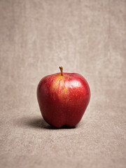 Red apple standing on textured beige background representing healthy food