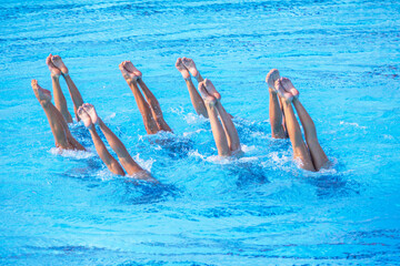 Artistic female swimming team performing synchronized legs movement in swimming pool