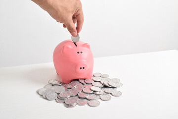 Hand putting coins into piggy bank isolated on white background with copy space. Saving, investment...