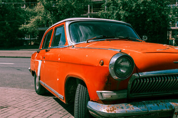 An old orange car is parked on a brick road