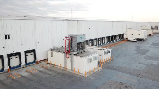 Drone footage capturing an aerial view of a modern warehouse facility. The video shows the exterior of a large, white warehouse building equipped with multiple loading docks.