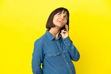 Pregnant woman using mobile phone isolated on yellow background and looking up