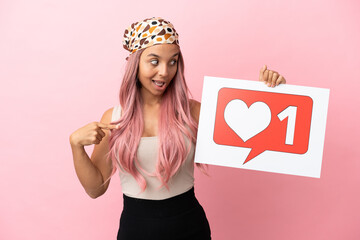 Young mixed race woman with pink hair isolated on pink background holding a placard with Like icon...