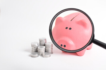 Saving Money with a Piggy Bank and a Magnifying Glass isolated on white background. Business...