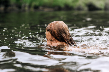 Fototapeta premium Little happy girl, child swims, dives in water on sea, in lake. Photo, portrait.