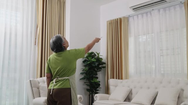 Handheld Shot Footage, A fatigued housekeeper in an apron cleans the house. Overheated, she switches on the air conditioning to cool off in the living room.