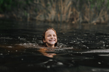 Fototapeta premium Beautiful smiling girl, happy child swimming in water, sea outdoors on summer holidays. Photography, portrait.