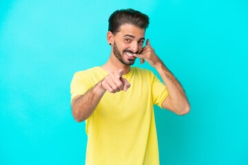 Fototapeta premium Young caucasian man isolated on blue background making phone gesture and pointing front