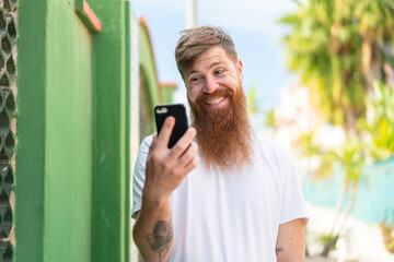 Obraz premium Redhead man with beard using mobile phone at outdoors with happy expression