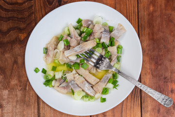 Sliced pickled herring with green onion and fork on dish