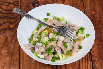 Sliced pickled herring with green onion and fork on dish 
