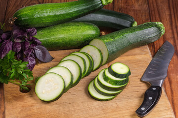 Sliced green zucchini on cutting board among the greens