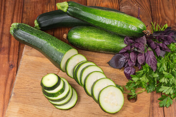 Sliced green zucchini on cutting board among the greens
