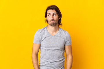 Young handsome man isolated on yellow background making doubts gesture looking side