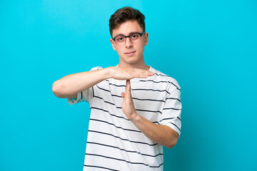 Young handsome Brazilian man isolated on blue background making time out gesture