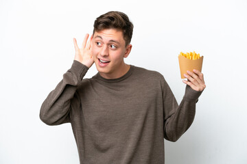 Young Brazilian man holding fried chips isolated on white background listening to something by...