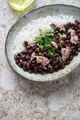 Bowl with black beans, chicken meat and white rice, vertical shot on a light-brown granite surface, middle close-up
