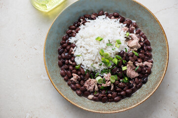 Plate of black beans with rice and chicken meat, horizontal shot on a light-beige stone surface, elevated view