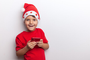 a boy in a Santa costume holds a smartphone in his hands. an emotional little santa. a cheerful child for Christmas with a phone.