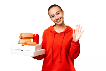 Young Arab woman holding fast food over isolated background saluting with hand with happy expression