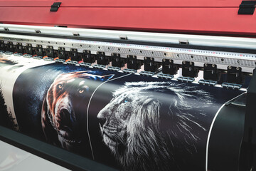 A large printer is printing a series of images, including a dog and a lion. The printer is black...