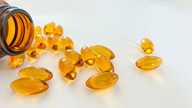 Soft gel capsules spilling from a brown bottle, featuring a translucent amber color, on a white background. Ideal for health, wellness, pharmaceutical, or vitamin supplement concepts