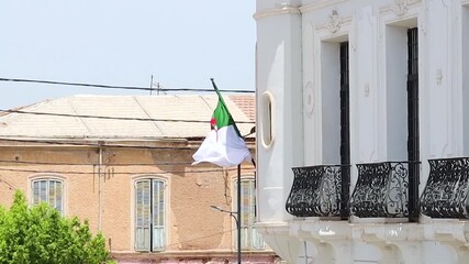 waving flag of algeria near house. symbol of the algerian people, african country, maghreb, green and red crescent moon with star