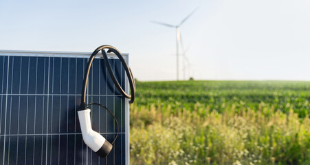 Close up of electric car charging plug with solar panel. Wind turbines in the background