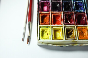 Well-used watercolor paint box with two brushes is shown, suggesting an artist is working on a creative project