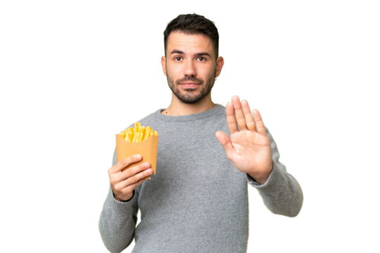 Young caucasian man holding fried chips over isolated chroma key background making stop gesture