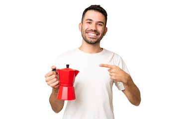 Young caucasian man holding coffee pot over isolated chroma key background and pointing it