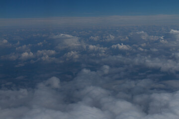 View from an airplane window showing the wing and engine against a backdrop of a vast expanse of clouds and a clear blue sky. The image captures the serene beauty of flight at high altitude.