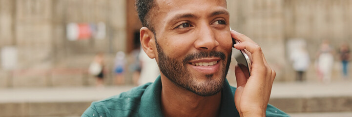 Obraz premium Happy young man sits on the steps of the Sagrada Familia in Barcelona, talking on smartphone