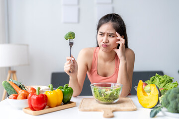 Young woman making disgusted face expression while holding fork with broccoli