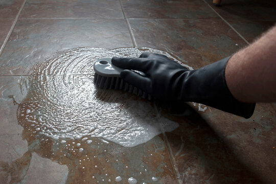 Person scrubbing kitchen floor tiles with a scrubbing brush and soapy water. Housework chore cleaning concept.