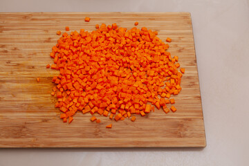 Carrot cut diced isolated on wooden cutting board on the kitchen table.