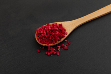 Crunchy pieces of Freeze dried raspberries in wooden spoon, close-up. Selective focus. Dehydrated raspberry berries. Delicious fruit topping for porridge, cereal, yogurt and desserts